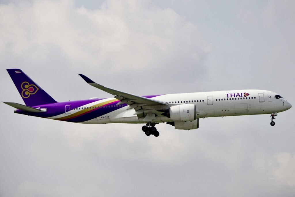 Thai Airways airplane flying in the sky with landing gear extended, cloudy weather.